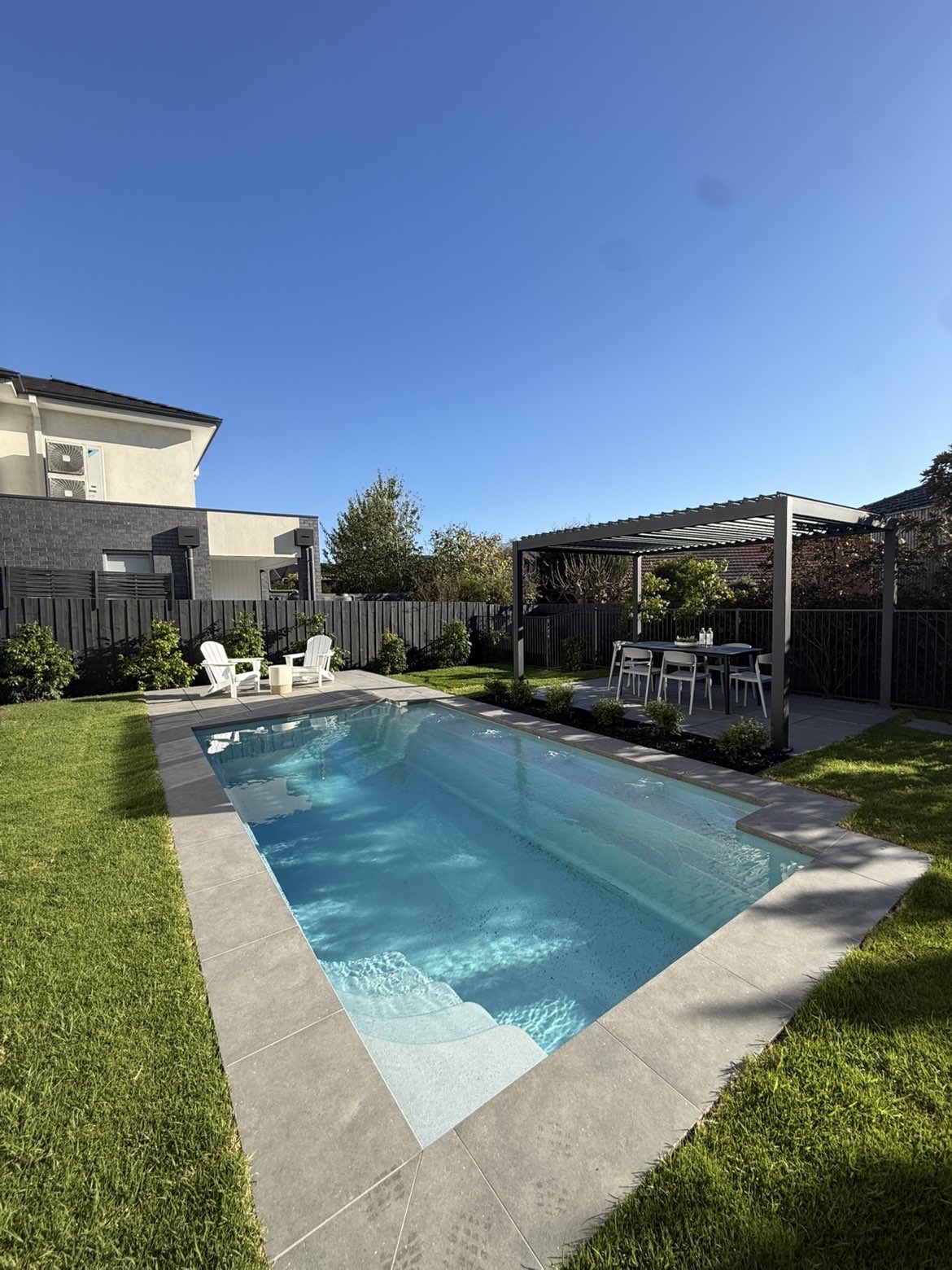 Dark metal roof structure over an outdoor dining area beside a pool