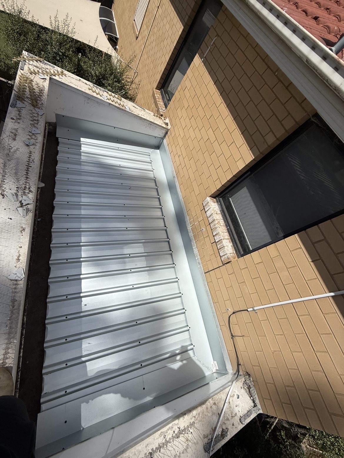 Metal roofing sheets and flashing installed beside a brick building