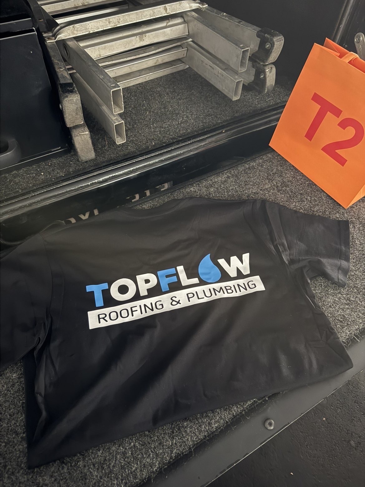 Topflow Roofing & Plumbing branded work shirt in the back of a work vehicle